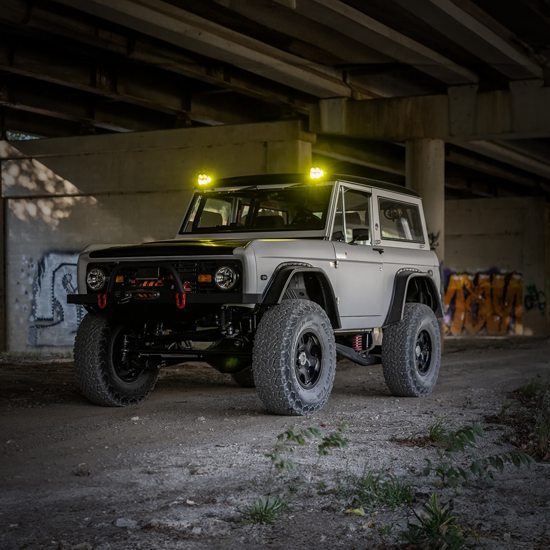 A rugged Ford Bronco with oversized tires parked under a bridge, its powerful stance accentuated by the urban graffiti backdrop