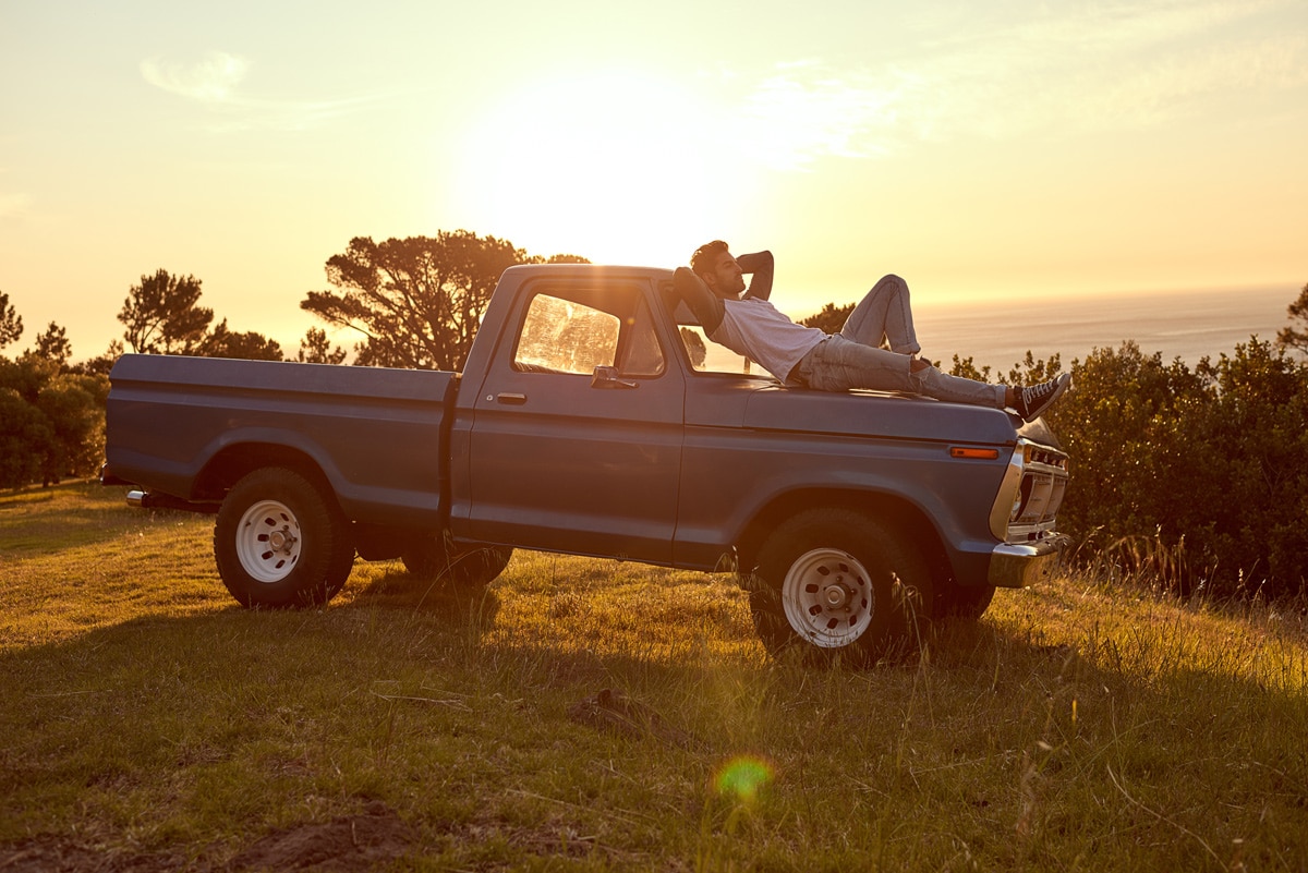 Young man laying on top of his vintage Ford F-series Trucks